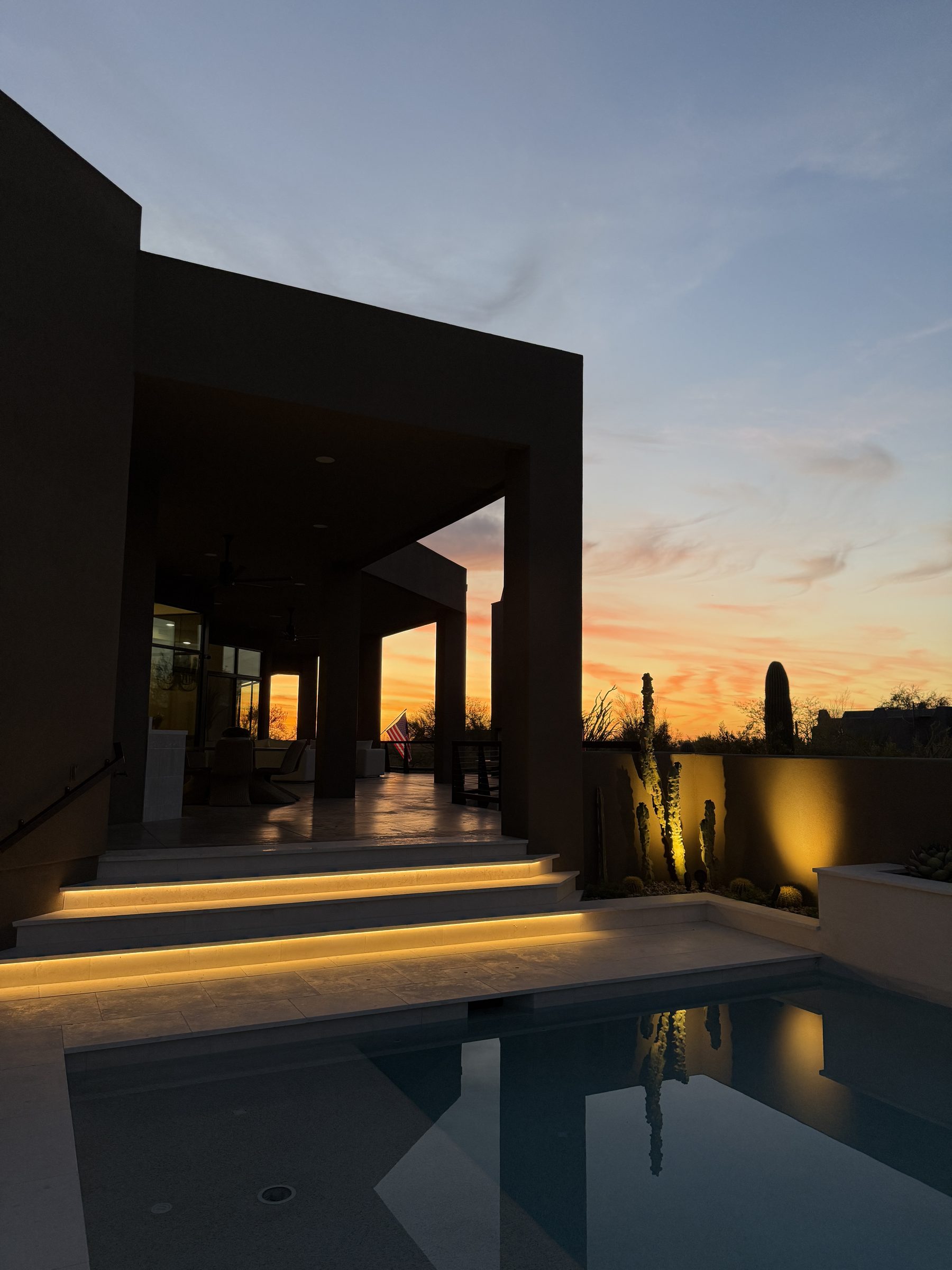 North Scottsdale residence at dusk — sunset through the dark entry portals, under-lit steps and saguaros