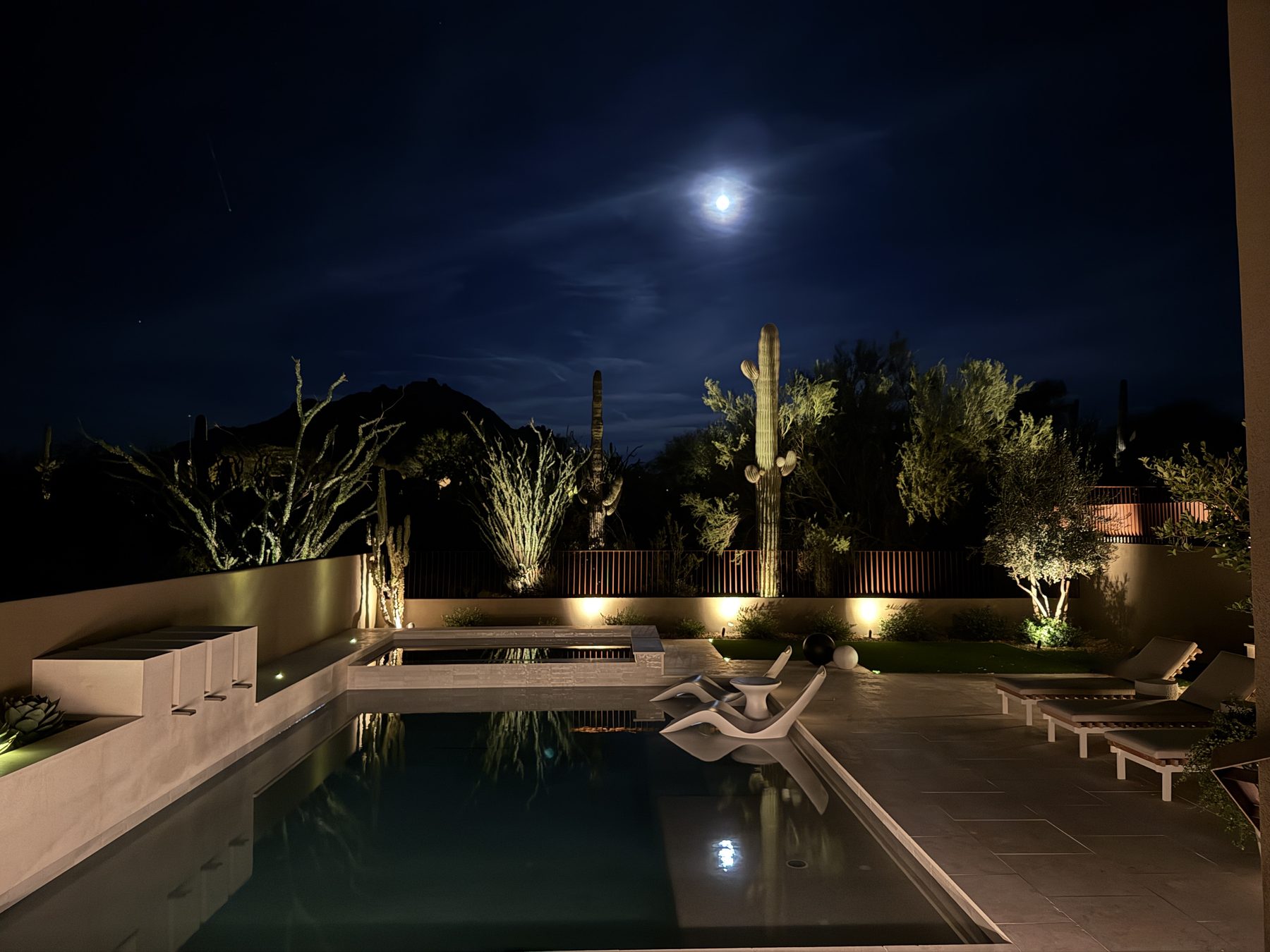 The same pool view after, by moonlight — raised spa, lit desert landscape and the expanded travertine deck