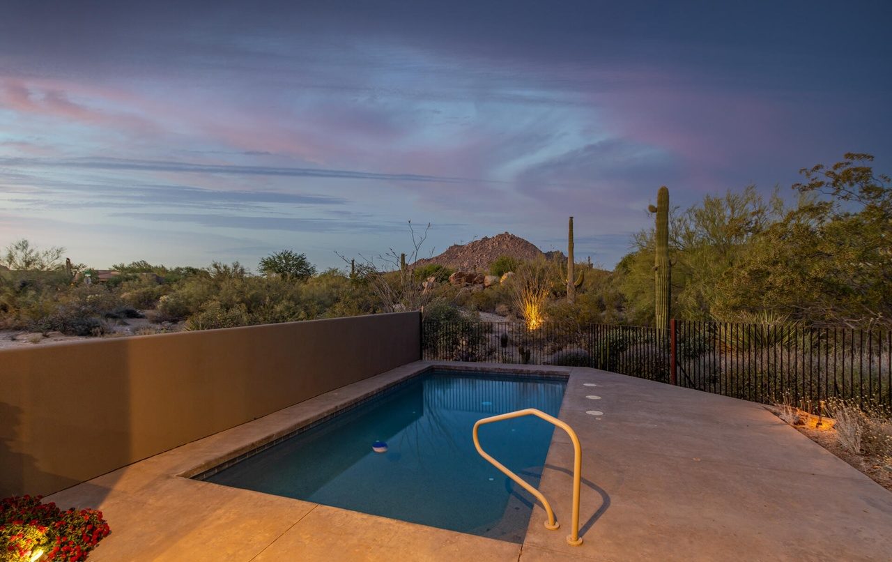 The pool at dusk as purchased, seen from the patio steps — bare concrete deck and a plain rectangular pool